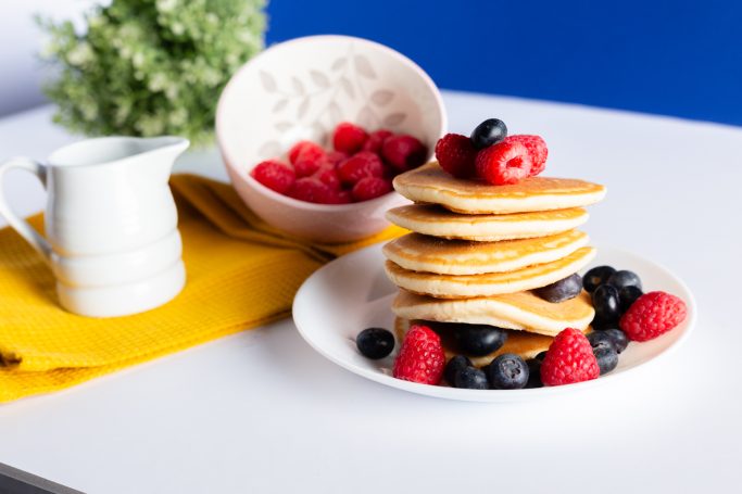 Stack of pancakes topped with raspberries and blueberries, with a small bowl of raspberries.