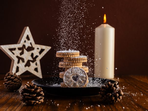 Cookies stacked on a plate with a candle, star decoration, and pine cones, dusted with sugar.