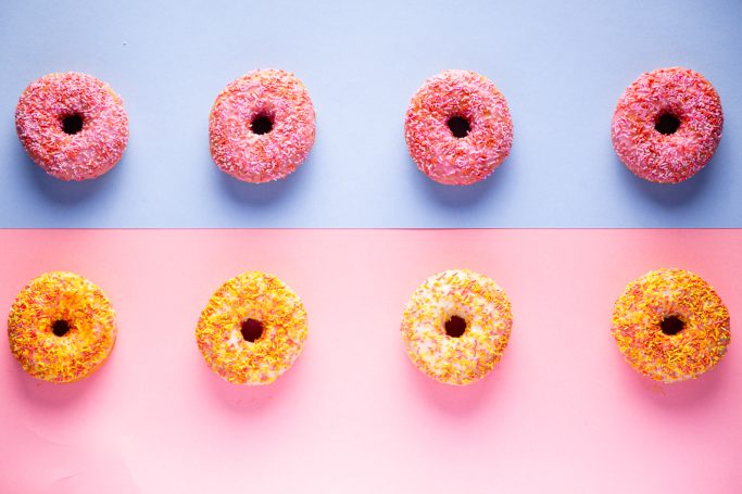 Three pink and three orange doughnuts with sprinkles, arranged in two rows.