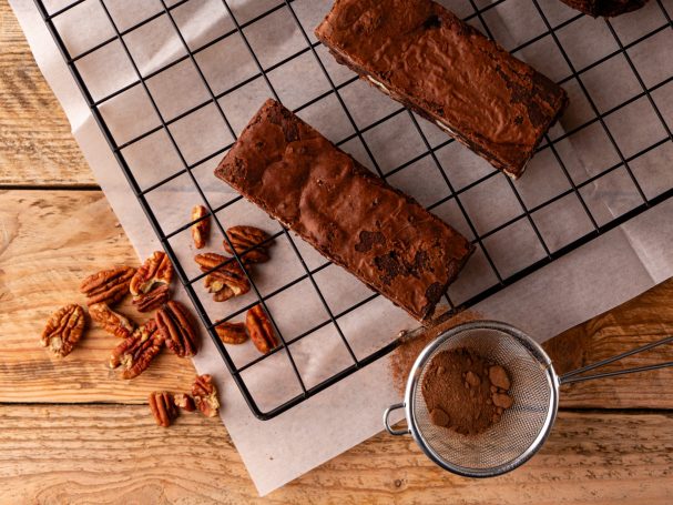 Decadent chocolate brownies on a cooling rack, with scattered pecans and cocoa powder.