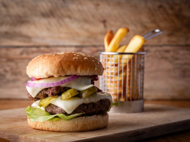 A burger with lettuce, cheese, onions, pickles, served with a side of fries.