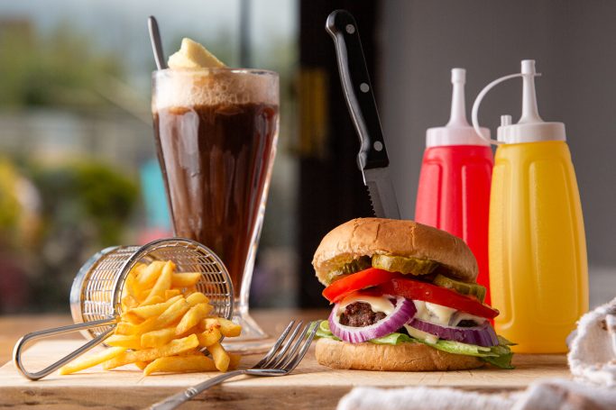 A burger with lettuce, tomato, and onion, served with fries and a fizzy drink.